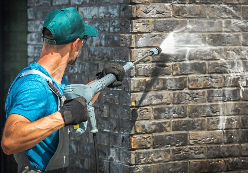 man power washing the brick concrete wall